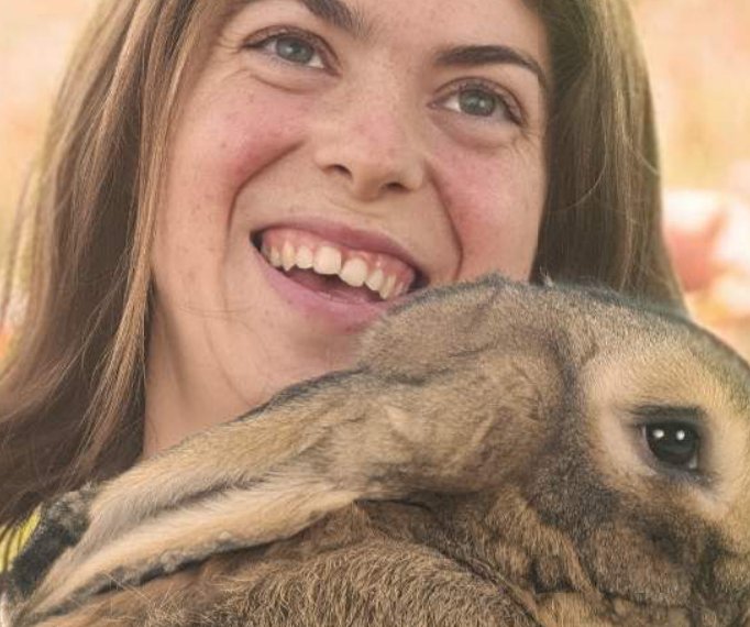 A woman smiling while holding a large Flemish Giant rabbit